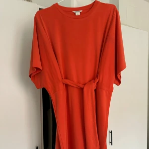 Orange klänning från Monki - Säljer en snygg orange (mer korallfärgad IRL) klänning från Monki i storlek XS. Klänningen har korta ärmar och ett knytband i midjan. Tyget känns tungt och exklusivt. Passar mig som vanligtvis har strl S. Köparen står för frakt ✨