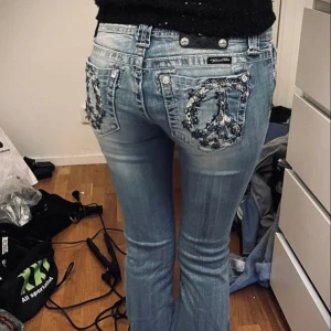 Miss me jeans peace sign - Snygga blå jeans från Miss me med unika broderade detaljer på bakfickorna. De har en tight passform och är perfekta för vardags. Jeansen har en klassisk femficksdesign och en low waist. Perfekt för dig som vill sticka ut lite extra!