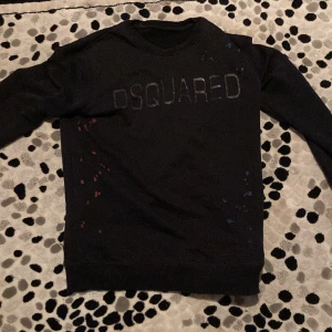 Svart tröja från Dsquared2 - Säljer en svart tröja från Dsquared2 med coola färgstänk och märkesnamnet diskret på bröstet. Tröjan har långa ärmar och är perfekt för en avslappnad stil. Passar både till vardags och fest. Skön och stilren!