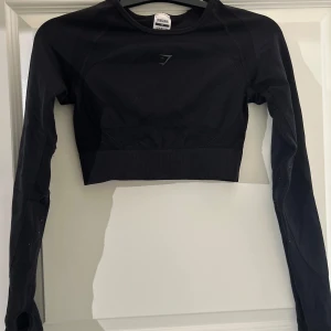 Svart långärmad croppad topp från Gymshark - Säljer en svart långärmad croppad topp från Gymshark. Perfekt för träning med sin tighta passform och stilrena design. Toppen har en liten öppning på ryggen och Gymshark-loggan tryckt baktill. Superbekväm och snygg för gymmet eller en aktiv vardag! Se tights för komplett set.