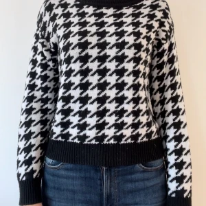 Svartvit stickad tröja med hundtandsmönster - Säljer en superfin svartvit stickad tröja med klassiskt hundtandsmönster. Tröjan har långa ärmar och en bekväm passform med ribbade muddar vid ärmslut och nederkant. Perfekt för både höst och vinter!