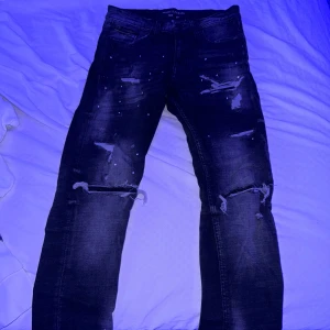 Svarta jeans från Supply & Demand - Säljer ett par svarta jeans från Supply & Demand i storlek XS. De har en cool distressed look med slitningar och hål på benen. Perfekta för en avslappnad och trendig stil. Jeansen har en knappstängning och är tillverkade i ett slitstarkt material.