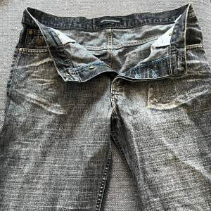 Säljer ett par grå jeans från Dolce & Gabbana. De har en cool, sliten look med ljusa tvättade detaljer. Jeansen har knappar framtill och klassiska fem fickor. Perfekta för en avslappnad stil!