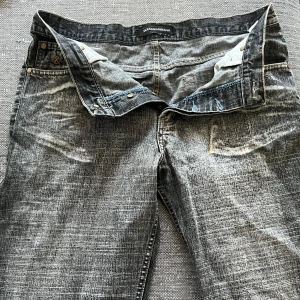 Grå jeans från Dolce & Gabbana - Säljer ett par grå jeans från Dolce & Gabbana. De har en cool, sliten look med ljusa tvättade detaljer. Jeansen har knappar framtill och klassiska fem fickor. Perfekta för en avslappnad stil!
