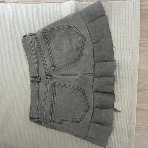 Grå jeanskjol med volang - Säljer en superfin grå jeanskjol med volangdetaljer. Kjolen är perfekt för både vardag och fest. Den har två stora fickor bak och en knapp framtill. ❤️ Jag köpte den från en annan tjej på Plick men den var för stor så jag säljer den❤️Storlek xs-s🫶🏼