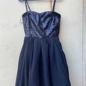 Svart paljettklänning från VILA - Säljer en superfin svart klänning från VILA i storlek M. Den har en glittrig paljettöverdel och en flödande kjol. Klänningen är axelbandslös med smala axelband och passar perfekt för festliga tillfällen. Den är i nyskick och redo för nästa äventyr!