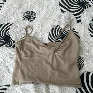 Beige linne med smala axelband - Säljer ett enkelt och stilrent beige linne med smala axelband. Perfekt för sommardagar eller som ett basplagg i garderoben. Linnet är i ett mjukt och bekvämt material.