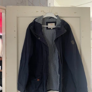 Mörkblå jacka från North Bend - Säljer en snygg mörkblå jacka från North Bend. Den har en randig insida och en huva för extra skydd mot väder och vind. Jackan är perfekt för höst och vår, med en stilren design och praktiska fickor. Den har en dragkedja framtill och en liten logga på bröstet. Passar perfekt för en casual look!