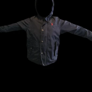 Svart jacka med huva - Säljer en mörkblå höstjacka med huva och knappar framtill från Polo - Ralph Lauren. Den har en liten röd logga på bröstet och är perfekt för höstvädret. Jackan har långa ärmar och två fickor framtill. Passar både till vardags och fest.