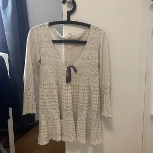  Spetsblus med knytband från Odd Molly  - Charmig beige/vit spetsblus med v-ringning och knytband framtill. Blusen har trekvartsärmar och ett vackert spetsmönster som ger en romantisk känsla. Perfekt för vår och sommar!