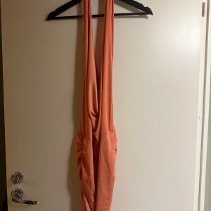 Orange klänning med kedjedetalj - Trendig orange klänning med kedjedetalj och rynkad design. Perfekt för en somrig look med sin ärmlösa stil och mjuka material.