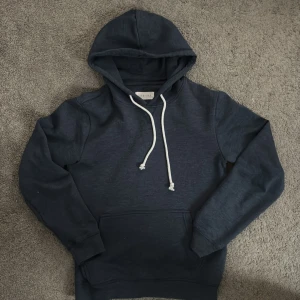 Mörkblå hoodie från Pier One - Säljer en stilren mörkblå hoodie från Pier One. Den har en klassisk design med justerbar huva och vita snören. Perfekt för en avslappnad look.