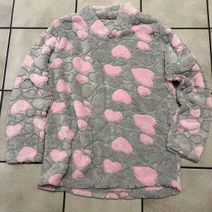 Grå och rosa fleece tröja med hjärtan - Mysig och fluffig grå fleece tröja med rosa hjärtmönster. Perfekt för kalla dagar när du vill känna dig extra bekväm och varm. Tröjan har långa ärmar och en avslappnad passform.