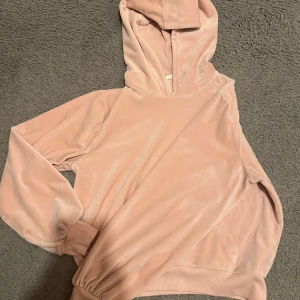 Rosa hoodie i sammet - Mysig rosa hoodie i mjukt sammetstyg. Perfekt för en avslappnad stil med långa ärmar och en bekväm huva.
