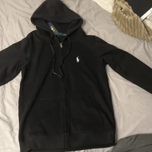Svart hoodie från Polo Ralph Lauren - Snygg svart hoodie från Polo Ralph Lauren med dragkedja och huva. Storlek m men är ganska liten i storlek så passar även dig med storlek s