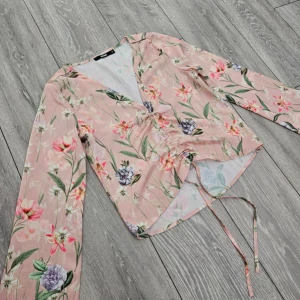 Blommig blus - Säljer en söt blommig blus från BikBok i rosa med gröna och vita och lila blommor. Blusen har en v-ringning och långa ärmar samt knytning framtill för en justerbar passform. Storlek XS men passar även S. Mycket bra skick!🌺🍸