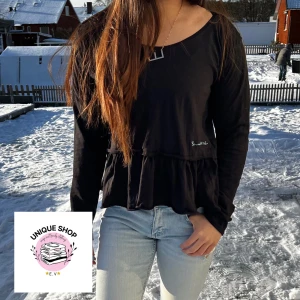 Svart långärmad topp med volangdetalj - Snygg svart långärmad topp med volangdetalj i nederkant. Perfekt för en stilren look med en twist. Toppen har en rund halsringning och är tillverkad i ett mjukt material. Wowsiii 🩵🩵