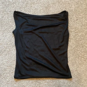 Svart topp från Jus de Pom - Ärmlös off shoulder topp med elegant passform. Skulle säga storlek S men materialet är stretchigt så skulle säkert passa M också. Silkigt material.