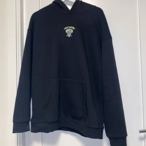 Svart hoodie med tryck från Your Turn - Säljer en svart hoodie från Your Turn med ett roligt tryck av en tecknad figur och texten 'I Hate Everyone'. Hoodien har en klassisk design med känguruficka och huva. Perfekt för en avslappnad stil.