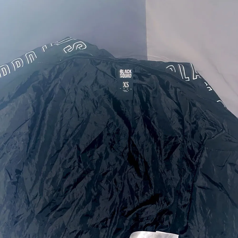 Snygg svart jacka från Black Squad med textdetaljer på ärmarna. Jackan har dragkedja framtill och praktiska fickor med dragkedjor. Perfekt för en cool och avslappnad stil.. Takit.