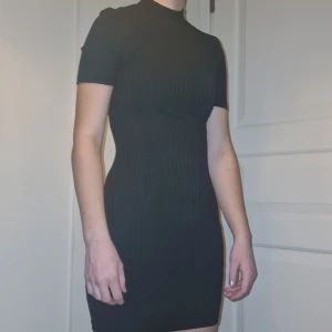 Svart ribbad klänning - Snygg svart ribbad klänning med korta ärmar och en tight passform. Perfekt för en stilren look. Köpt begagnad, aldrig använd av mig. Passar xs-s.