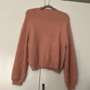 Rosa fluffig tröja - Mysig rosa tröja med fluffig textur och rund hals. Perfekt för kyliga dagar med sin varma och bekväma design. Långärmad och ribbad vid ärmslut och nederkant.