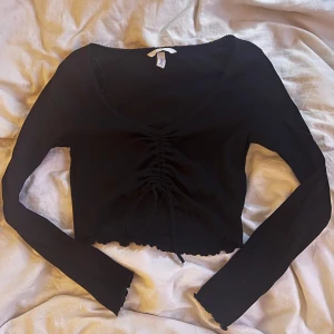 Svart långärmad topp från H&M - Snygg svart långärmad topp från H&M med knytning framtill. Toppen är croppad och har en stilren design som passar perfekt till olika tillfällen.