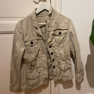 Beige jacka med knappar - Säljer denna beiga jackan med detaljer! Funkar för både tjej och kille. Använd ca två gånger, inga defekter! Som nyskick förutom att den är lite skrynklig. Kom privat vid frågor!💕Skulle säga Strl.S