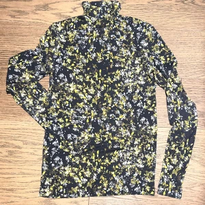 Mönstrad polotröja från COS - Snygg polotröja från COS med ett unikt mönster i svart, gult och vitt. Tröjan har långa ärmar och en hög krage, perfekt för att ge en stilren look. Passar utmärkt för både vardag och speciella tillfällen. Stretchig och skön, något liten i storleken. 