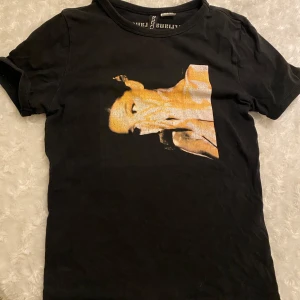 Svart t-shirt från H&M Divided - Snygg svart t-shirt från H&M Divided med ett tryck av en guldfärgad bild på framsidan. Perfekt för en casual look.