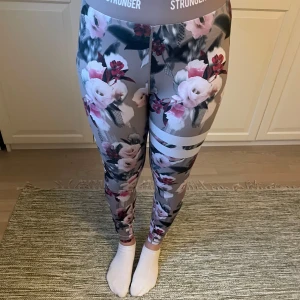 Blommiga leggings från Stronger - Snygga leggings från Stronger med ett blommigt mönster i rosa och grå toner. De har en hög midja och är tillverkade i ett stretchigt material som består av polyester och elastan. Perfekta för träning eller en avslappnad dag.