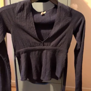 Mörkblå  topp från Nelly - Säljer en mörkblå topp från Nelly med v-ringning och långa ärmar. Toppen har ett knytband i midjan för en snygg passform. Perfekt för en stilren look!