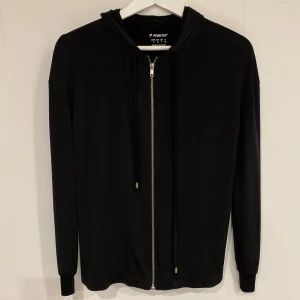 Svart träningströja från Work Out - Säljer en stilren svart tröningströja från Work Out. Tröjan har dragkedja framtill och långa ärmar, perfekt för träning eller vardagsbruk. Tillverkad i träningstyg.