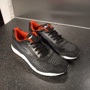 Oanvända löparskor - Svarta löparskor med röda detaljer och vit sula. Skorna har snörning och en bekväm passform, perfekt för träning. Helt oanvända då dem va fel storlek. 