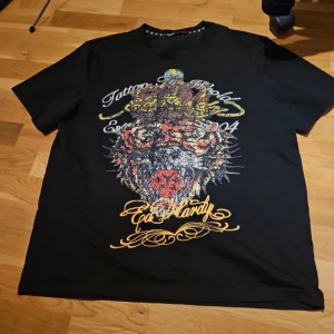 Svart t-shirt med tigertryck - Cool svart t-shirt med ett stort tigertryck i färgglada nyanser på framsidan. Textdetaljer i vitt och gult ger en extra touch. Defekter= paljetter ramlar av på framsidan (gäller ej baksidan).. ställ gärna fler frågor gällande varan! 