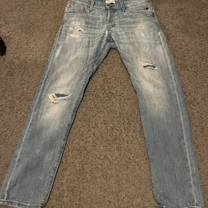 Blåa jeans med slitningar - Snygga blå jeans med slitningar på framsidan. De har en klassisk femficksdesign och en rak passform. Perfekta för en avslappnad stil. Modellen är slim/glenn