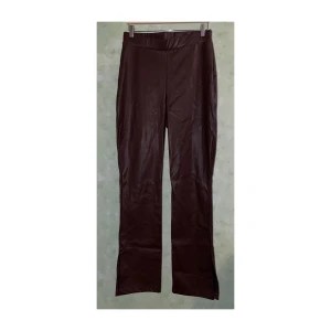 Nly Trend | Byxor | High waist | Faux-leather | Bruna | Stl. L - Bruna stretchiga high waist byxor i rak passform med slits i faux-leather/läderimitation. Finns dragkedja på sidan.  Storlek L  Ungefärliga mått: Midja: 80 cm Längd: 112 cm  I mycket bra använt skick! Finns endast mindre tecken på användning.