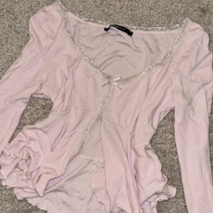 Ljusrosa topp från Gina Tricot - Säljer en söt ljusrosa topp från Gina Tricot i storlek XS. Toppen har långa ärmar och är dekorerad med spetsdetaljer och en liten rosett framtill. Den är även öppen vid magen som syns på bilden!🩷