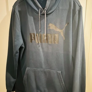Mörkblå hoodie  - Säljer en snygg mörkblå hoodie från Puma i storlek M. Den har en klassisk design med en stor Puma-logga på framsidan och en bekväm känguruficka. Perfekt för både vardag och chill. Huvan är justerbar med dragsko och materialet känns mjukt och skönt. Passar perfekt till höst och vår!