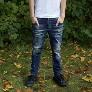 DSQUARED2 Ibrahimovic Icon  jeans - Blå - Blå jeans från Dsquared2 i samarbete med Zlatan Ibrahimovic. Medvetet slitna detaljer och färgstänk, knappar i gylfen. Hällor för bälte i midjan. Köpta Secondhand!!! Modellen 182 cm