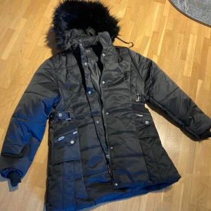 Ny täckjacka  - Oanvänd täckjacka med avtagbar huva, muddar i ärmslut och slejfar i midjan