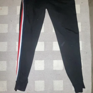 Svarta mjukisbyxor från Moncler - Snygga svarta mjukisbyxor från Moncler med en cool randig detalj i rött, vitt och blått längs sidan. Perfekta för en avslappnad stil med en touch av lyx. Byxorna har en bekväm passform och är gjorda i mjukt material.