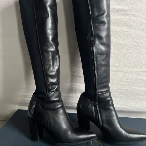 Svarta stövlar från Novita - Snygga svarta stövlar från Novita i skinn med hög klack och dragkedja på sidan. Perfekta för en stilren look. Stövlarna har en elegant design som sträcker sig över knäet. Superbekväma och passar till allt!  Använda fåtal gånger.  Nypris 2200:-
