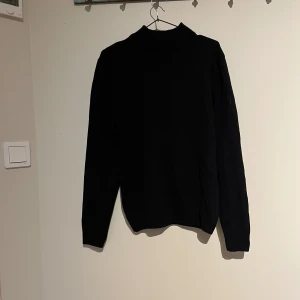 Svart polotröja från DeFacto - Säljer en stilren svart polotröja från DeFacto. Tröjan har en klassisk design med långa ärmar och en hög krage, perfekt för kyligare dagar. Den är tillverkad i ett mjukt material som ger en bekväm passform. Passar utmärkt till både vardag och mer uppklädda tillfällen.