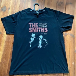 Svart T-shirt med The Smiths-tryck - Säljer en svart T-shirt med tryck av The Smiths. T-shirten har korta ärmar och ett vintage-inspirerat motiv på framsidan. Bra skick! 