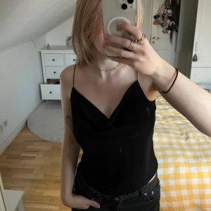 Svart linne - Snygg svart linnetopp med tunna axelband och draperad halsringning. Perfekt för en stilren look.