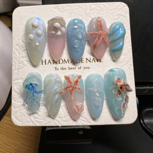 Handgjorda naglar med havstema - Unika handgjorda naglar med havstema, dekorerade med sjöstjärnor, bubblor och snäckor i pastellfärger som blått, rosa och pärlemor. Perfekt för en somrig look med en touch av havet.