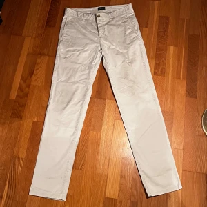 Beige chinos - Snygga beige chinos med normal passform och midwaist. Byxorna har en klassisk design med knappar och dragkedja framtill. Perfekta för en stilren look.