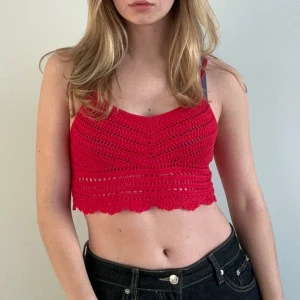 Röd virkad croppad topp - Säljer en snygg röd virkad croppad topp med smala axelband. Perfekt för sommardagar och ger en bohemisk känsla. Toppen har ett fint mönster och en vågig kant nedtill.