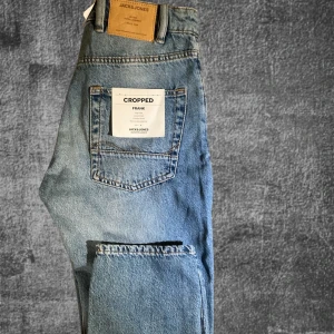 Blå Cropped Jeans från Jack & Jones - Säljer ett par snygga blå cropped jeans från Jack & Jones som är oanvända. De har en avslappnad passform och är perfekta för både vardag och helg. Jeansen har en klassisk femficksdesign och är tillverkade i slitstarkt denim. Perfekta för både vinter och vår